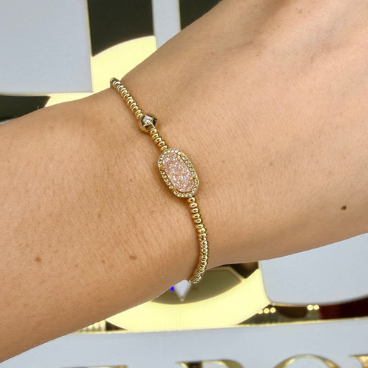 Gold bracelet on a wrist with a blurred background featuring decorative elements.
