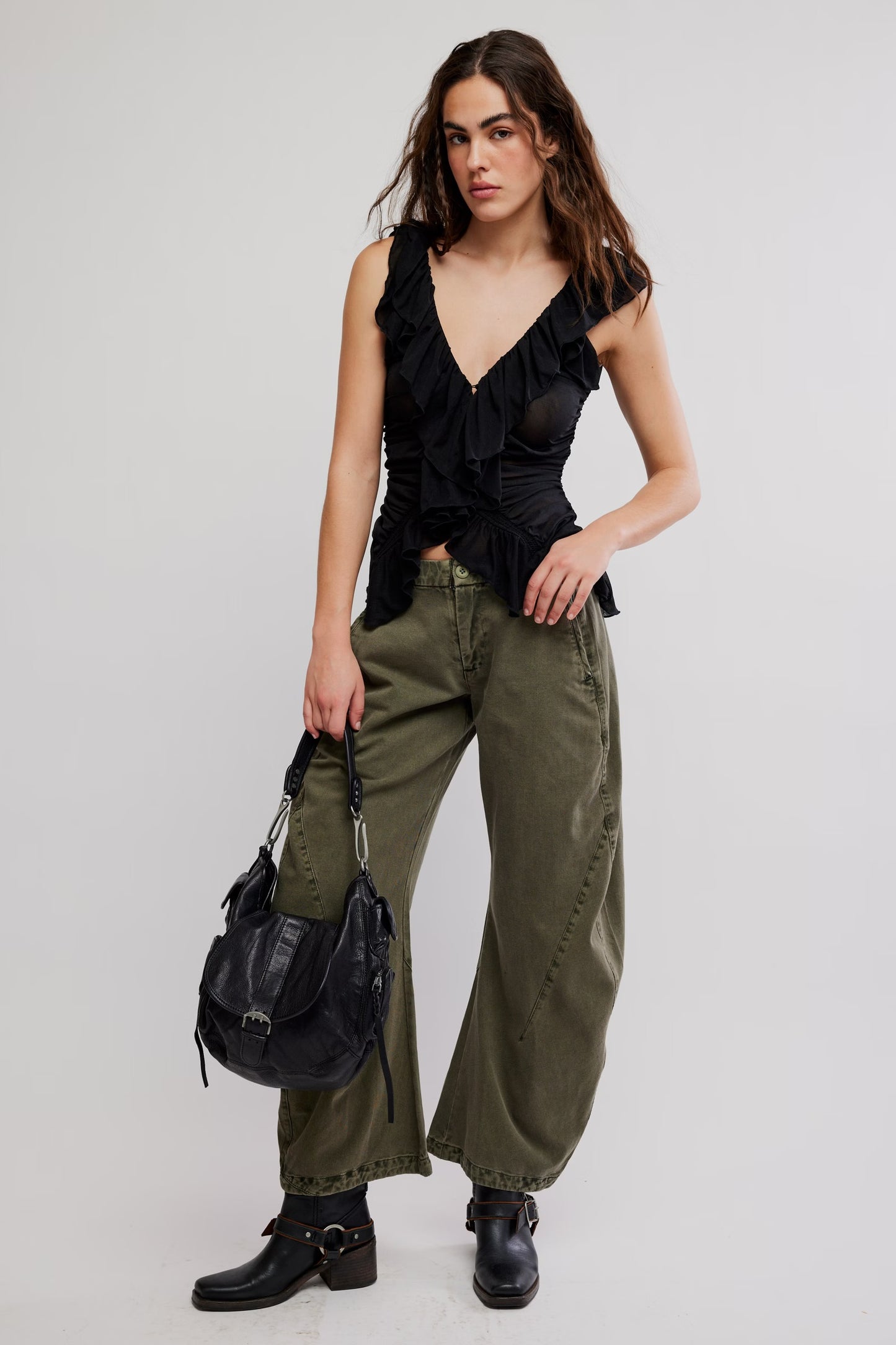 Model wearing black flowy tank top with green jeans facing forwards holding a black purse