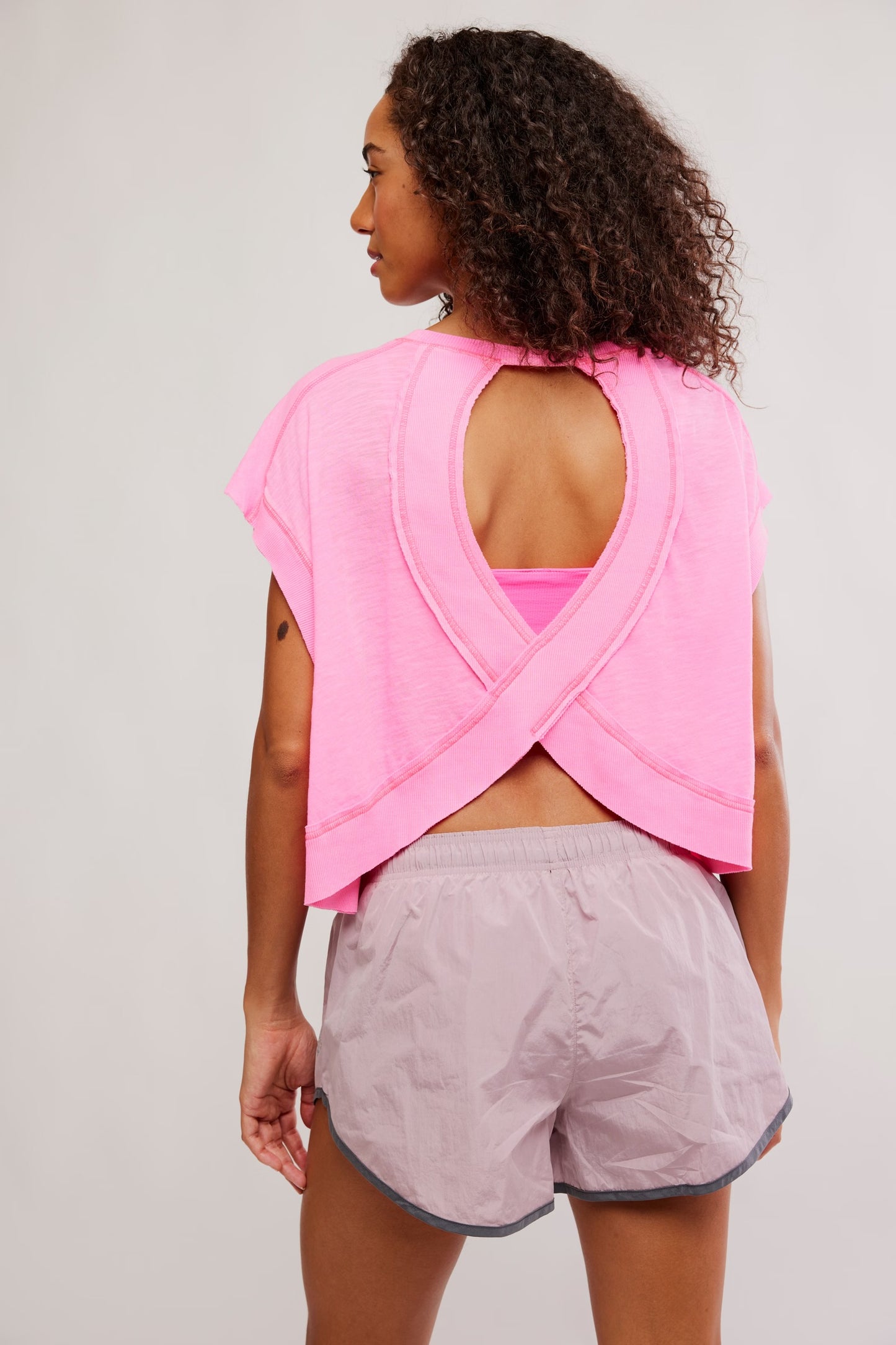 model wearing pink shirt with cutout and mauve shorts on a white background facing backwards