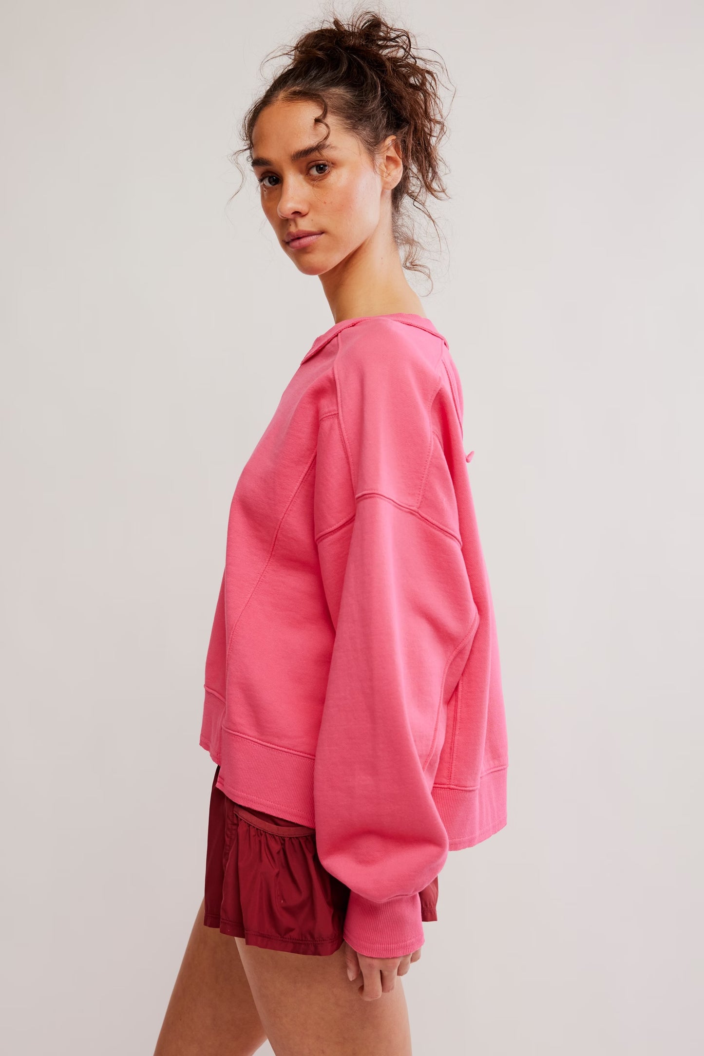 Person wearing a pink sweatshirt and red shorts on a plain background