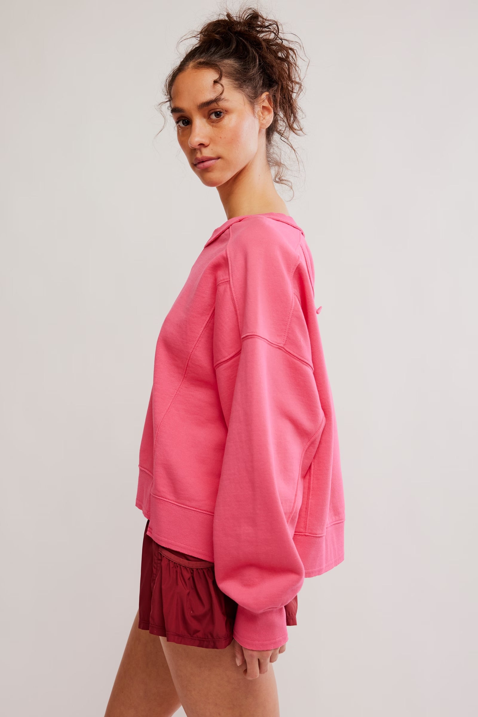 Person wearing a pink sweatshirt and red shorts on a plain background