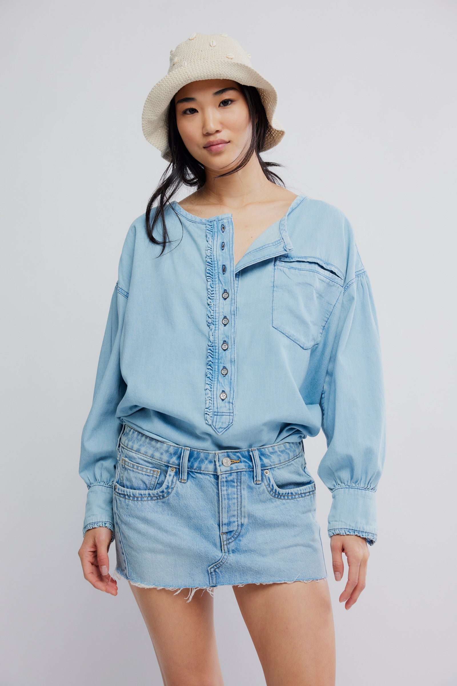Woman wearing a light blue denim outfit with a beige hat on a plain background