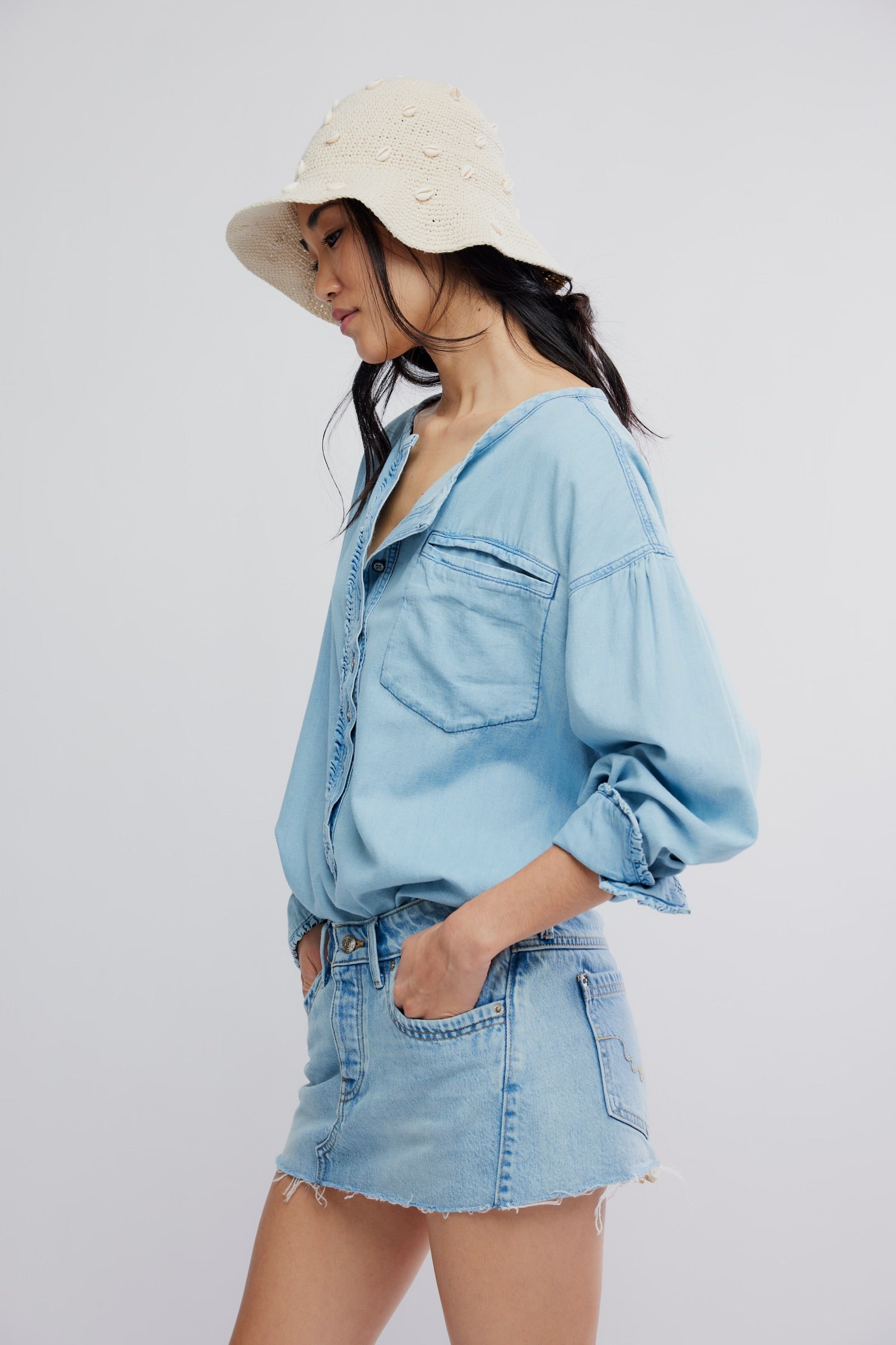 Woman wearing a light blue denim outfit with a white hat on a plain background