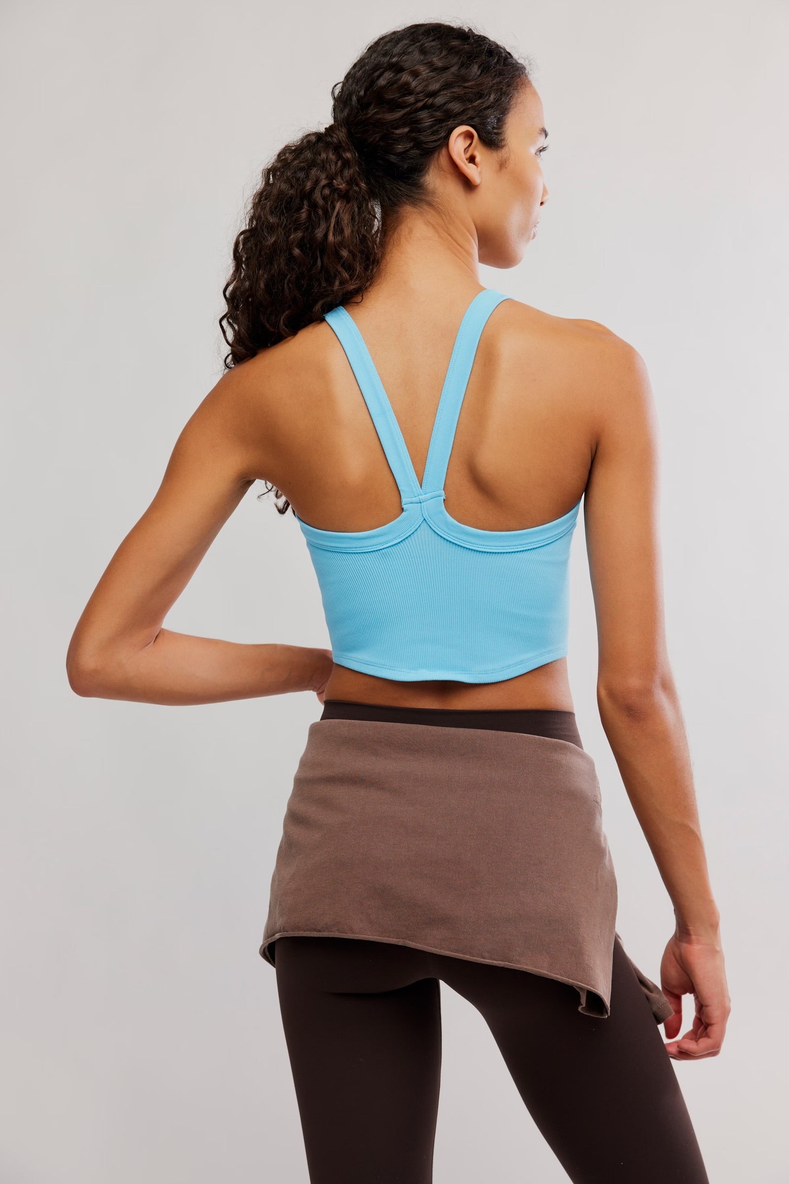 Woman wearing a blue sports bra and brown skirt on a plain background
