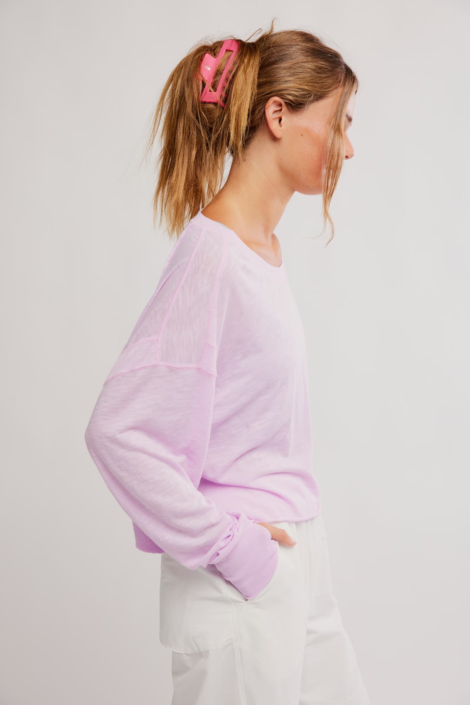 Woman wearing a light purple sweater and white pants against a plain background