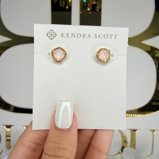 Hand holding a pair of earrings on a Kendra Scott card with a decorative background.