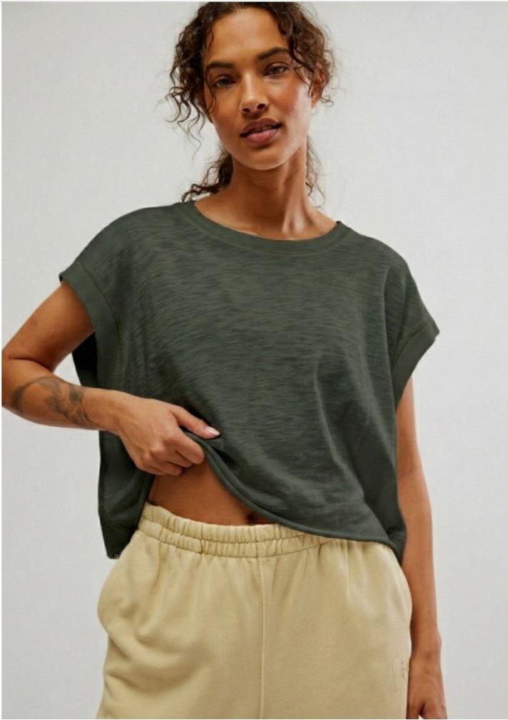 Woman wearing a green t-shirt and beige pants against a plain background