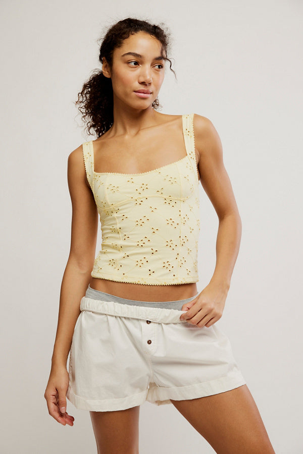 Woman wearing a light yellow lace top and white shorts on a plain background
