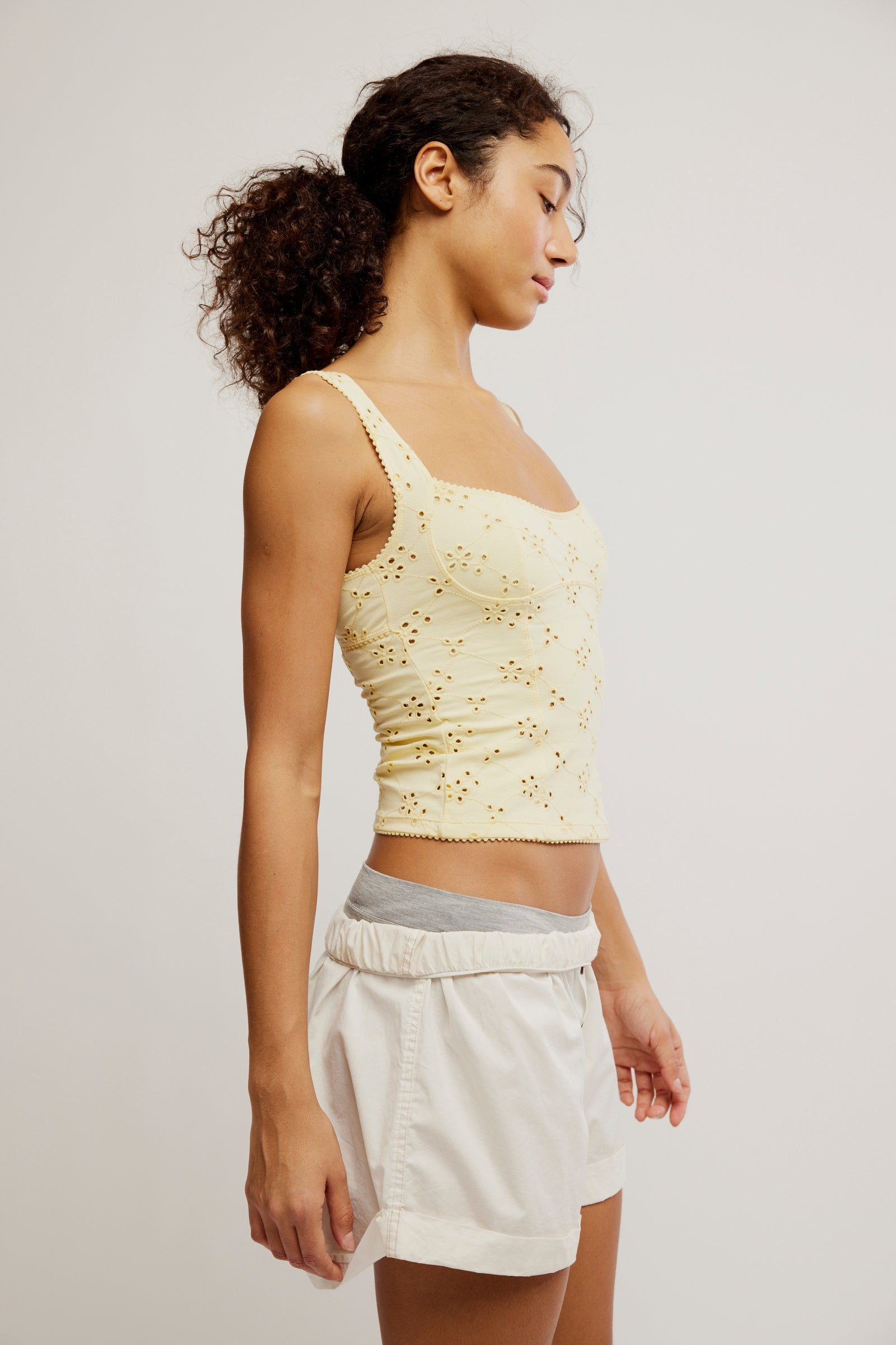 Woman wearing a light yellow lace top and white shorts on a plain background