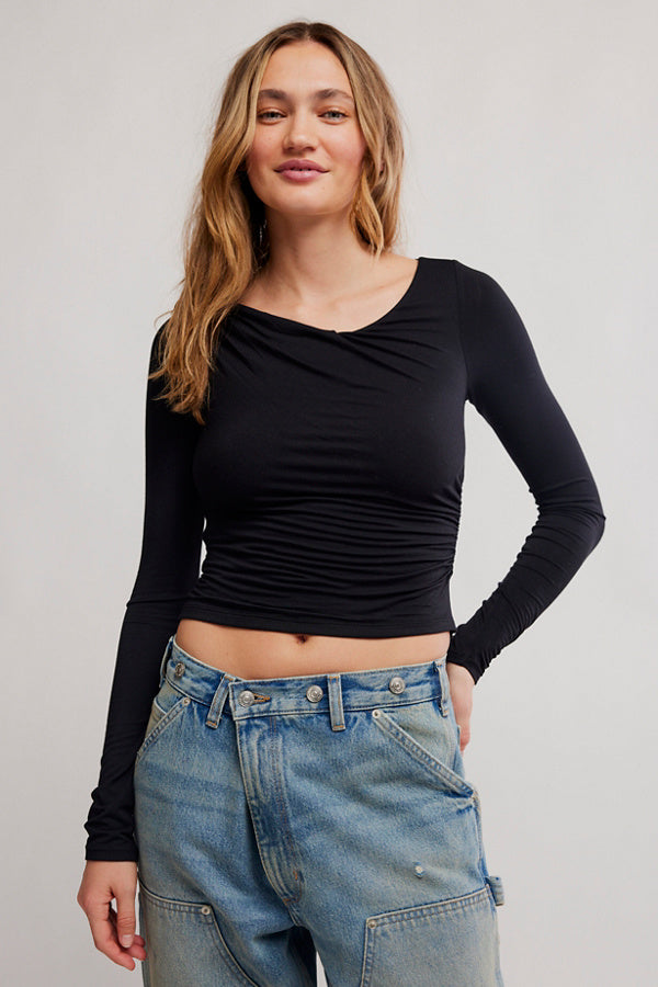 Woman wearing a black long-sleeve top and blue jeans against a plain background
