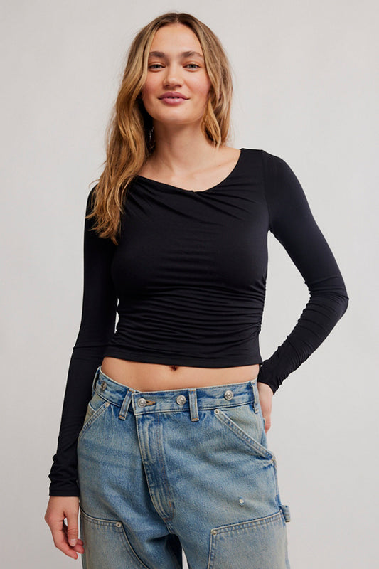 Woman wearing a black long-sleeve top and blue jeans against a plain background