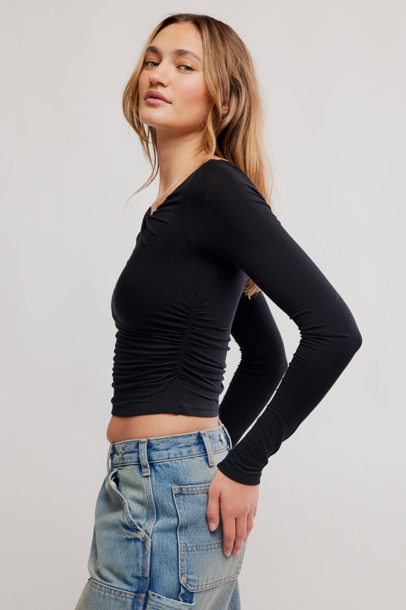 Woman wearing a black long-sleeve top and blue jeans on a light gray background