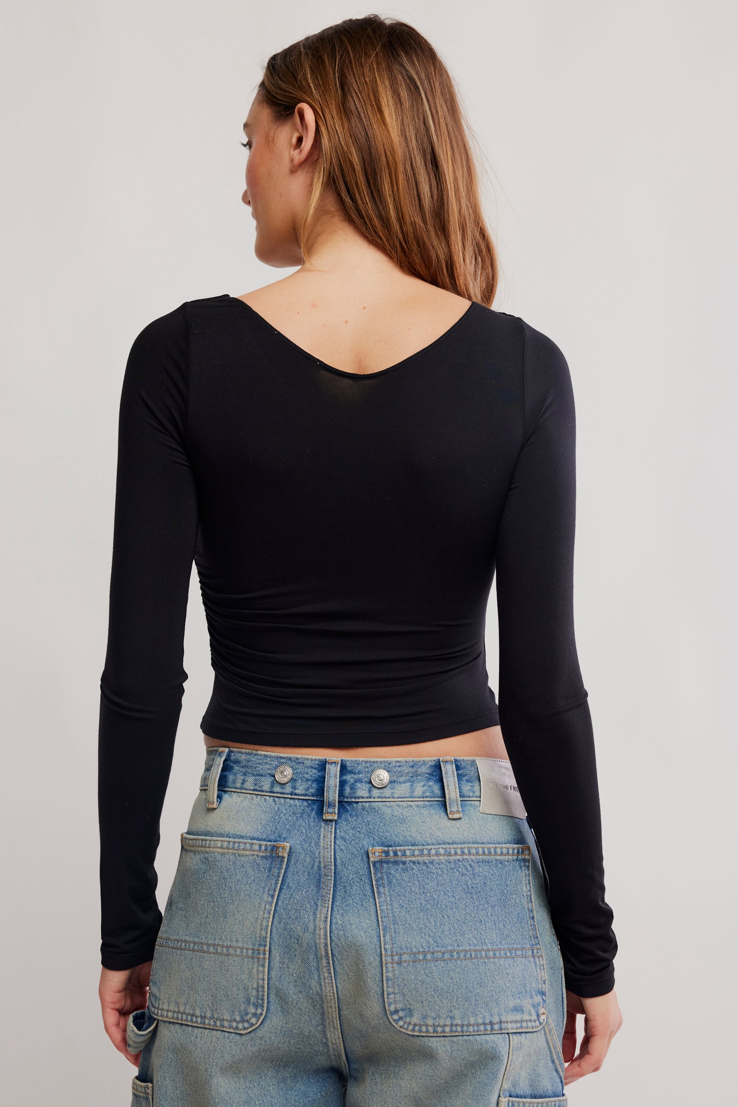 Person wearing a black long-sleeve top and blue jeans on a plain background