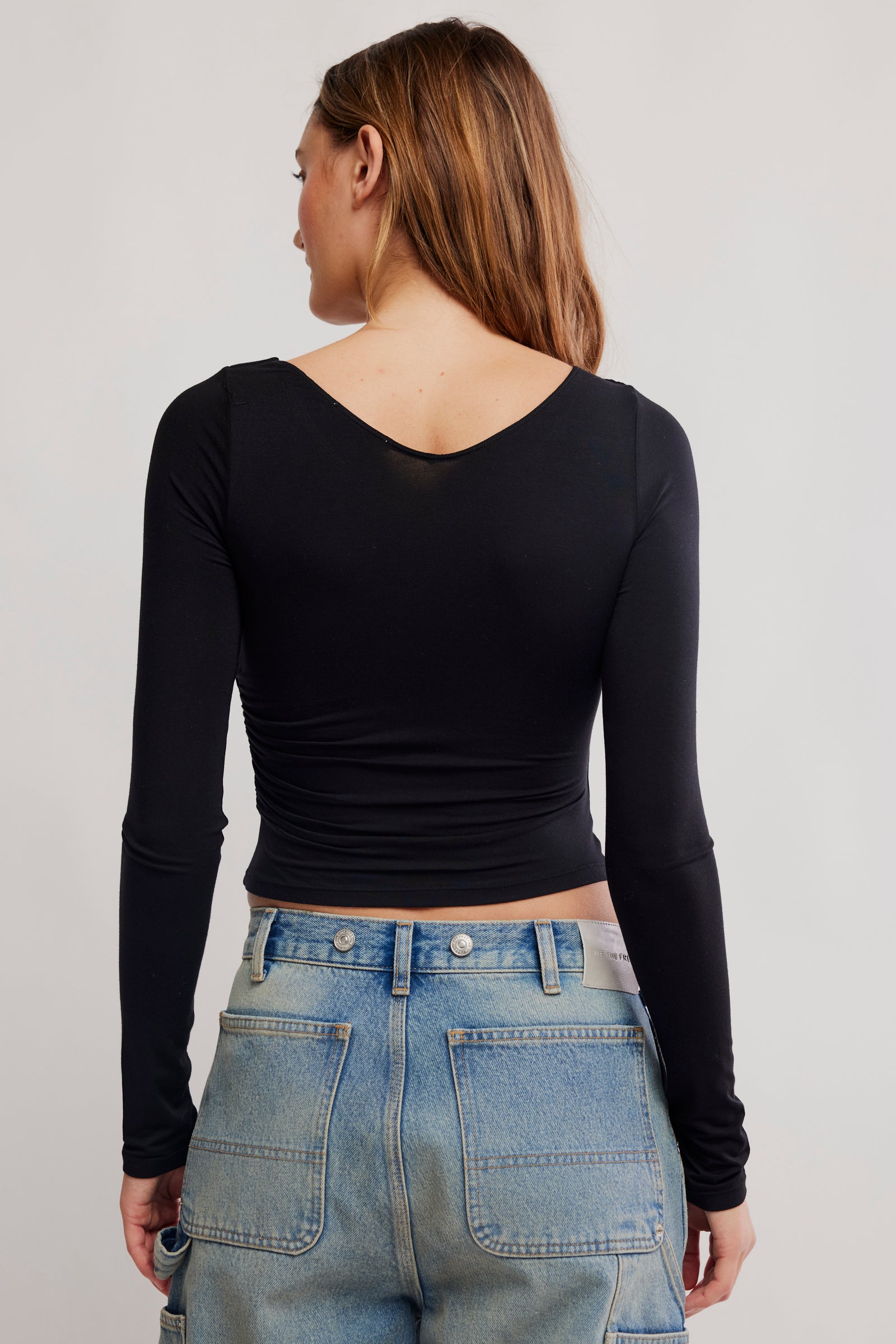 Person wearing a black long-sleeve top and blue jeans on a plain background