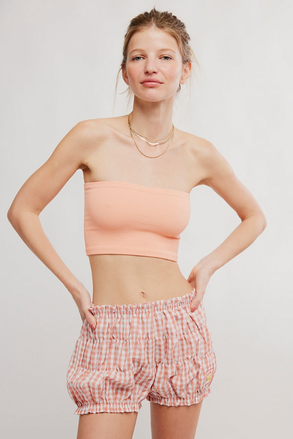 Woman wearing a peach top and checkered shorts on a plain background