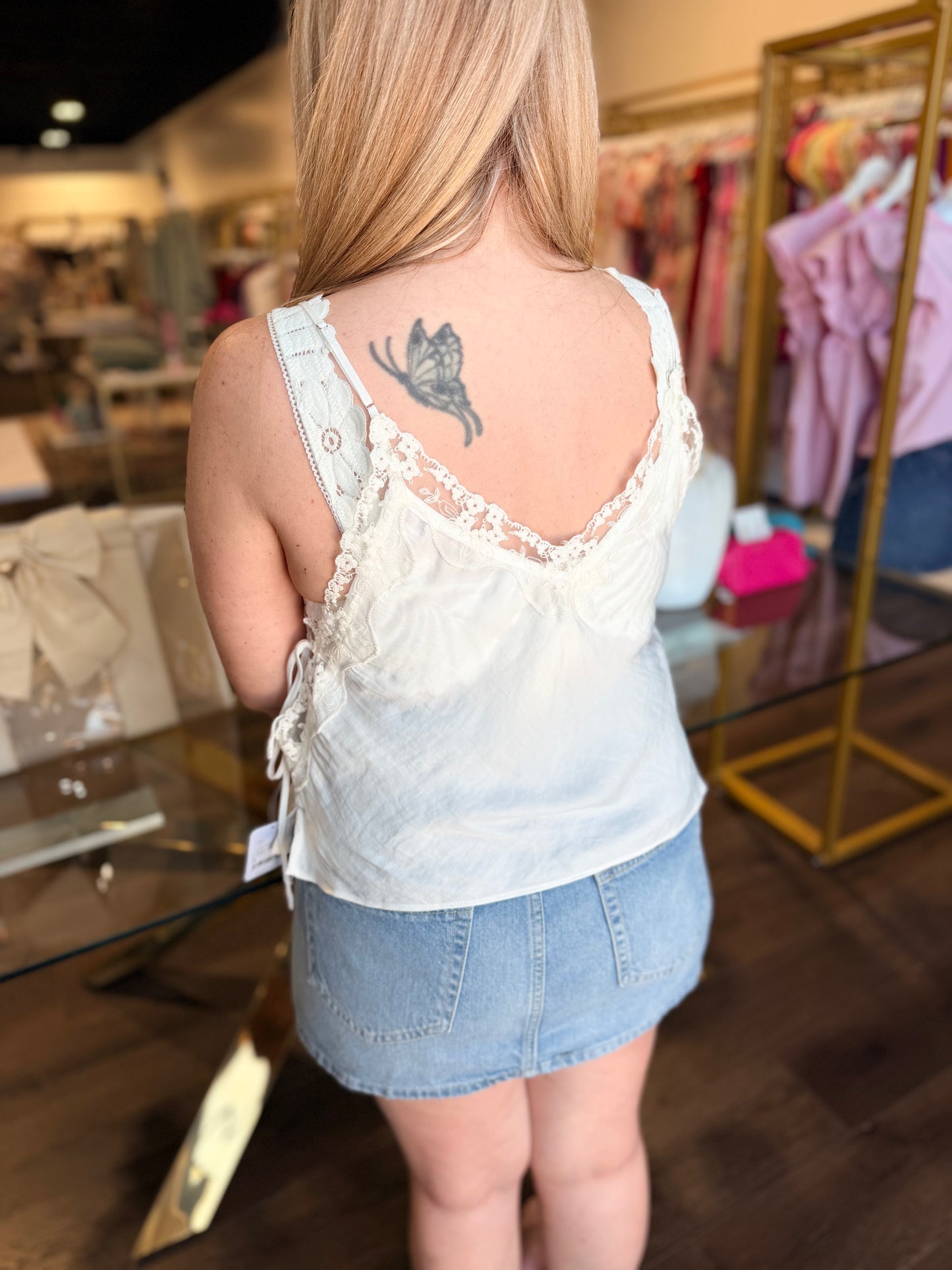 Woman wearing a light-colored tank top and denim skirt in a store setting.