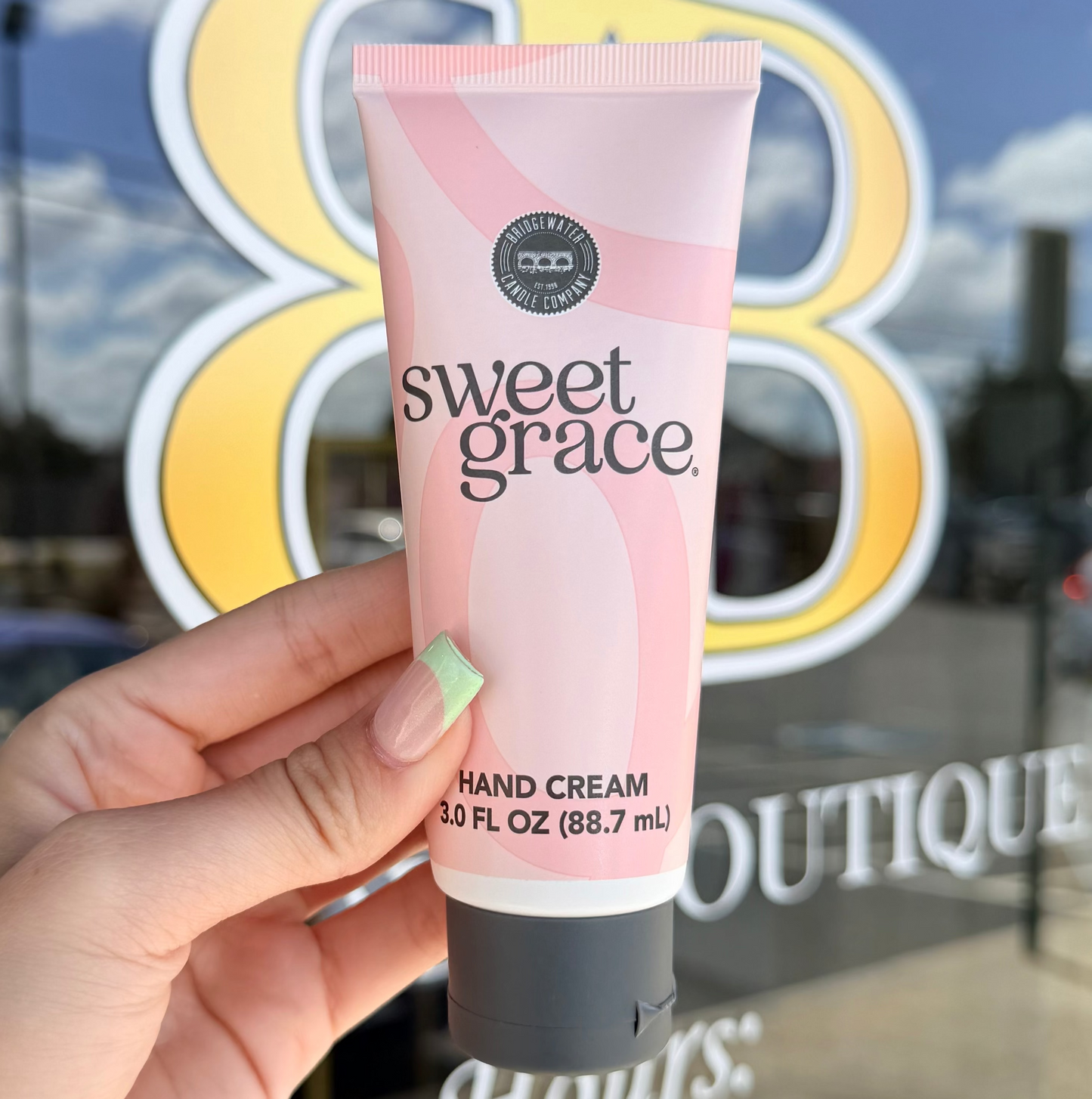 Hand holding a tube of Sweet Grace hand cream in front of a store window.