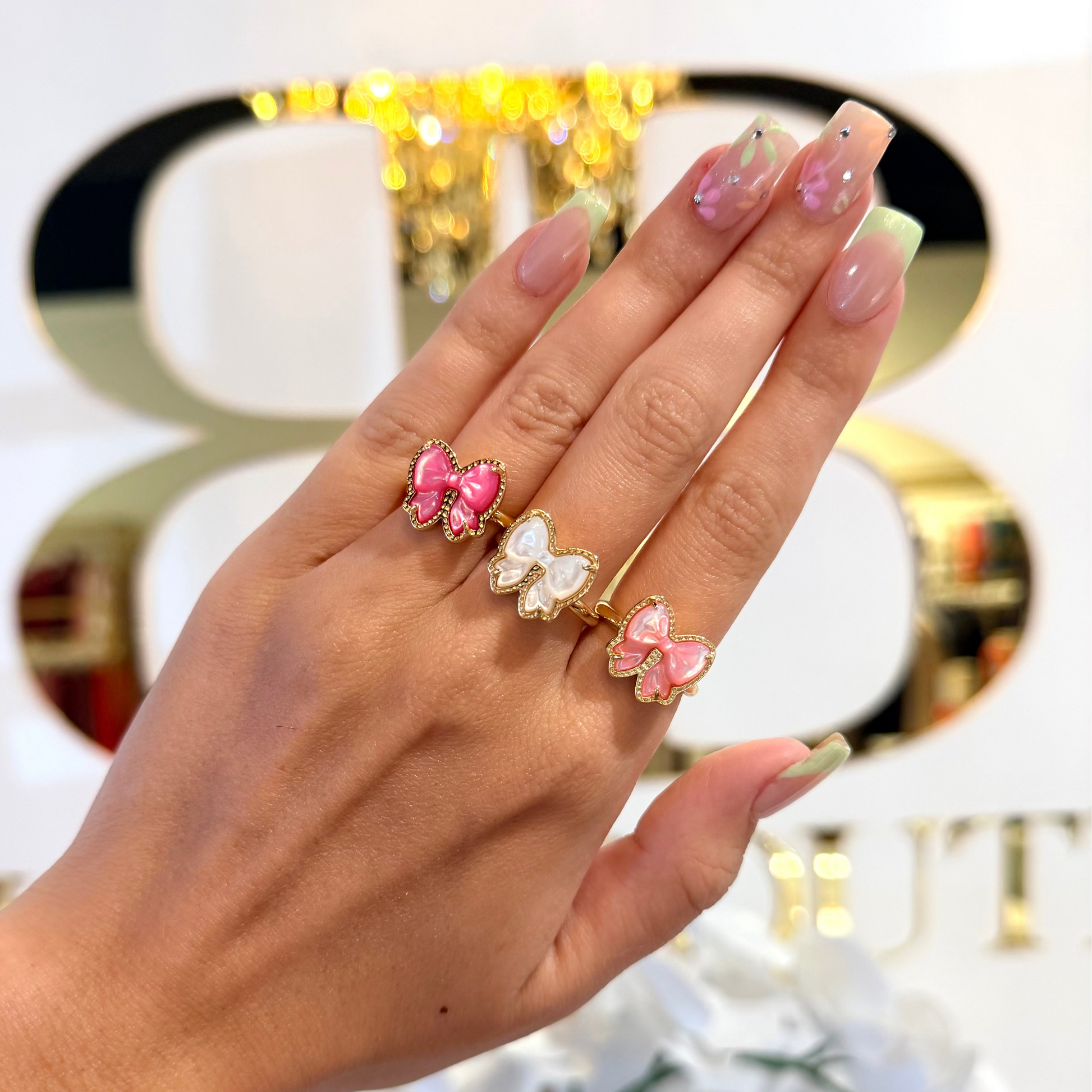 Hand wearing two pink bow rings with a blurred decorative background