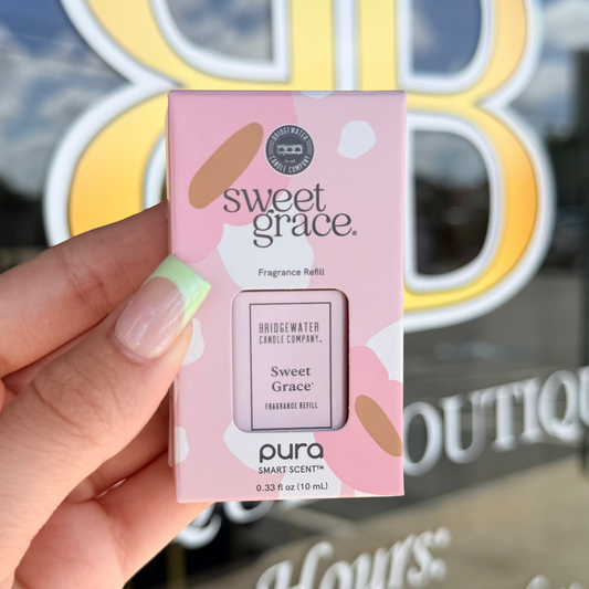 Hand holding a 'sweet grace' fragrance refill box in front of a store window.