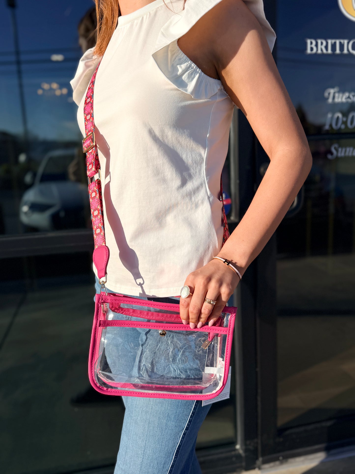 Person holding a clear handbag with pink strap in front of a store entrance.