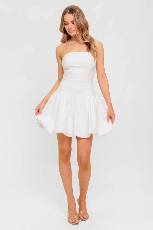 Woman wearing a white strapless dress against a plain background