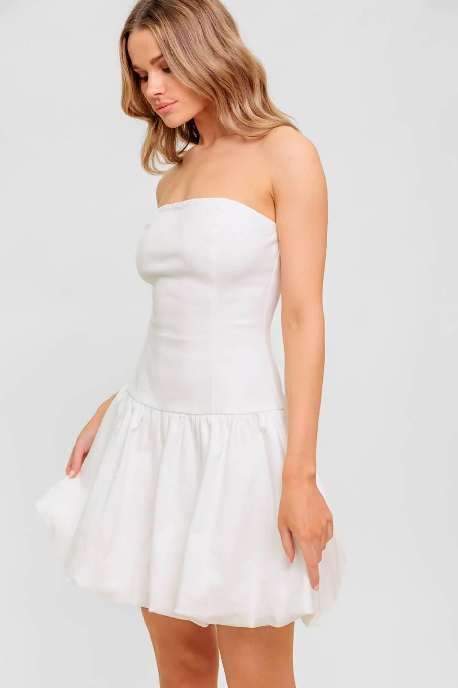 Woman wearing a strapless white dress against a plain background
