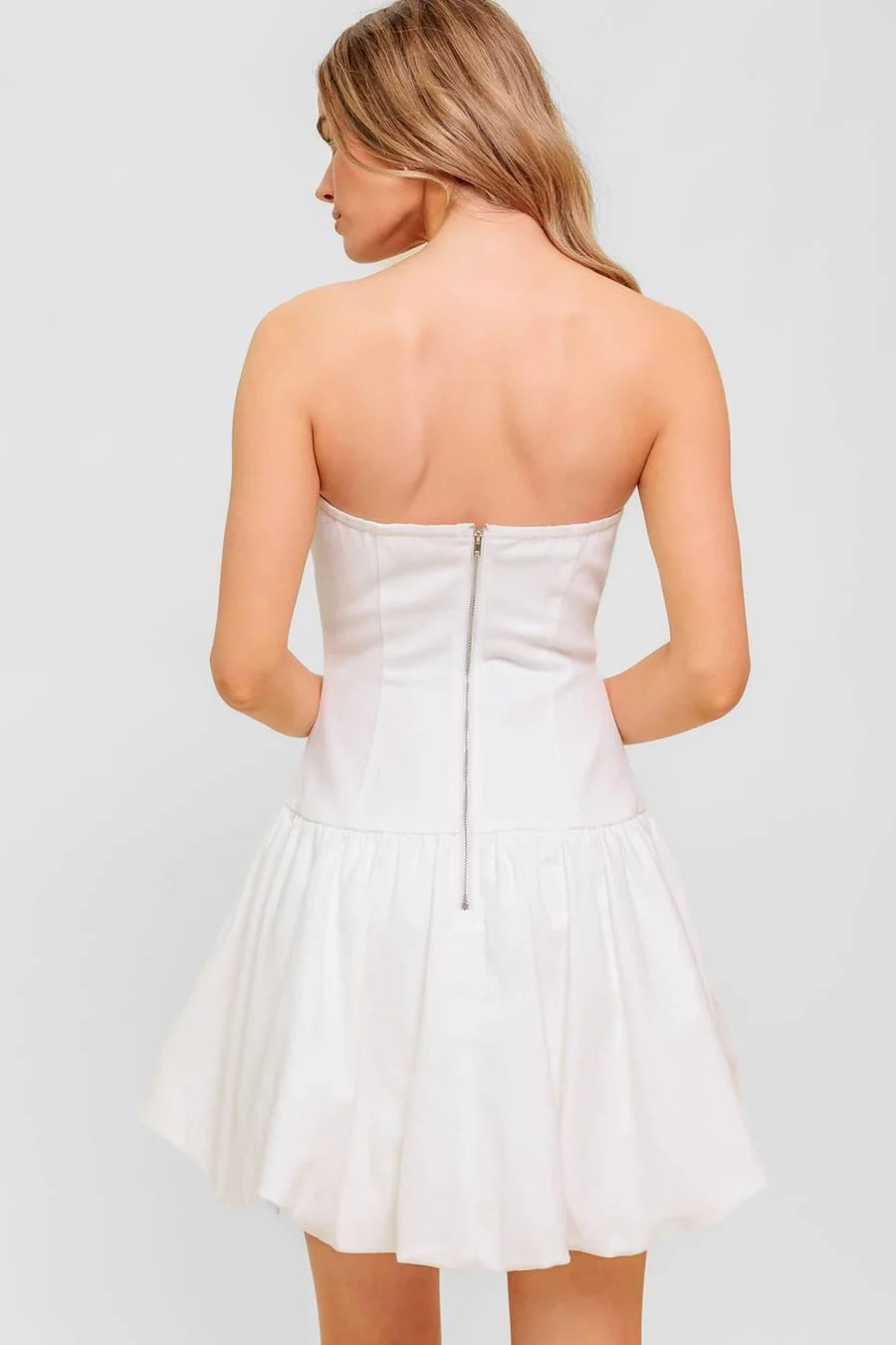 Woman wearing a white strapless dress against a light gray background