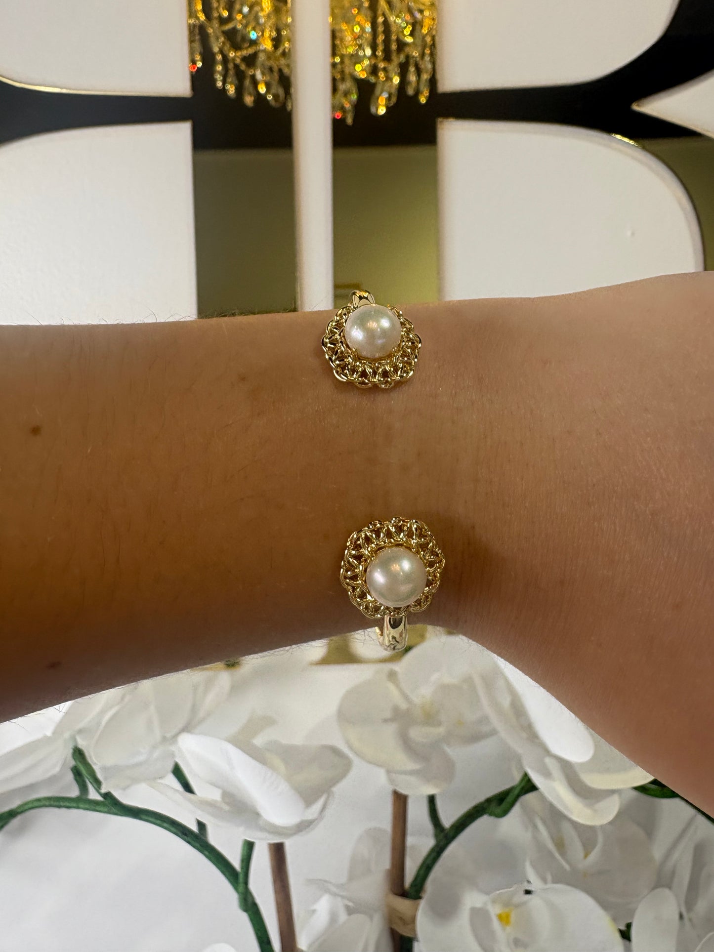 Gold KENDRA SCOTT bracelet with pearl-like stones on a wrist, with a decorative background.