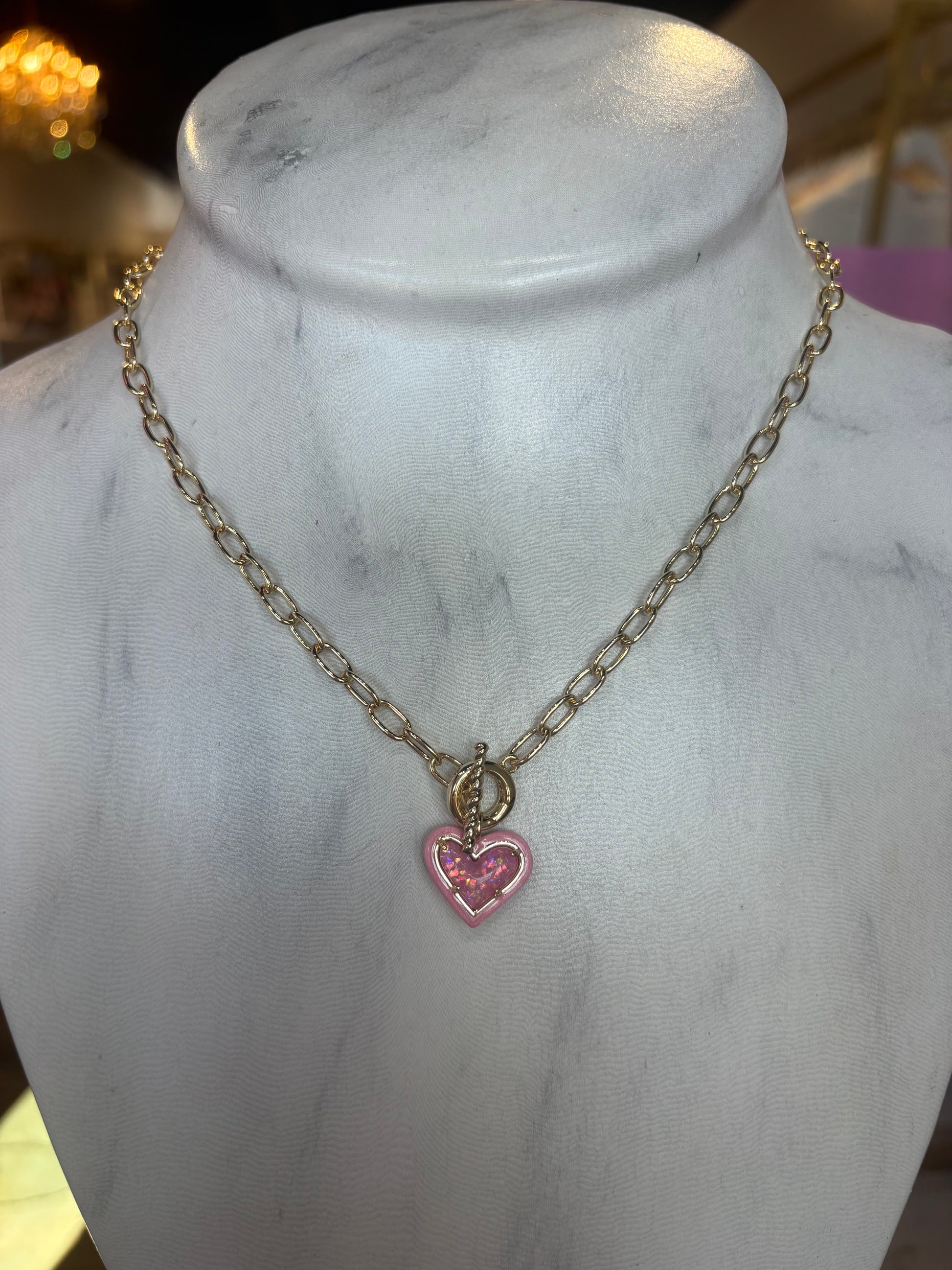 Gold Kendra Scott necklace with a pink heart pendant on a marble mannequin.