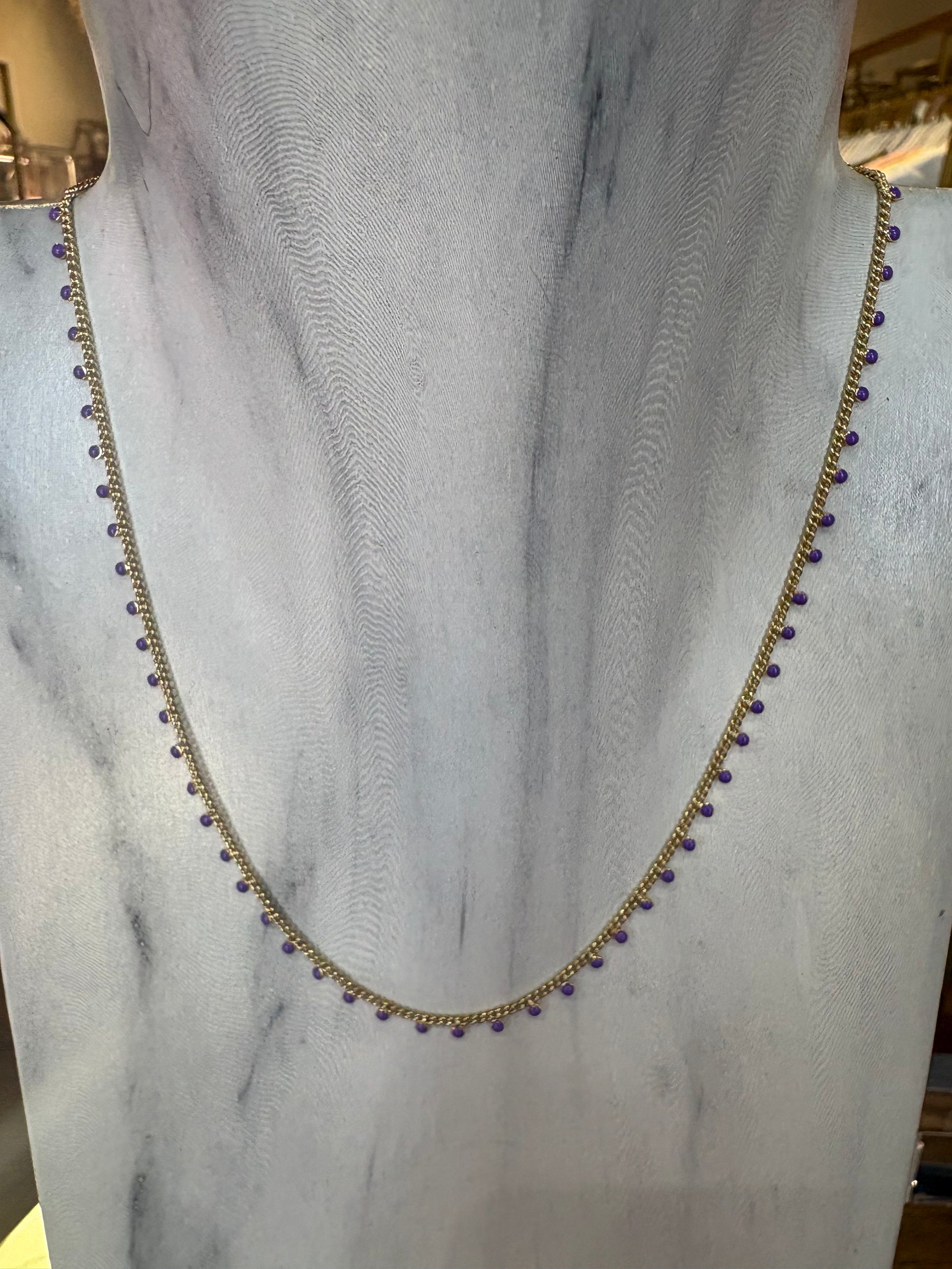 Gold KENDRA SCOTT necklace with purple beads on a marble surface.