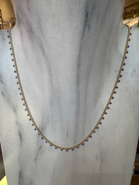 Gold KENDRA SCOTT necklace with purple beads on a marble surface.