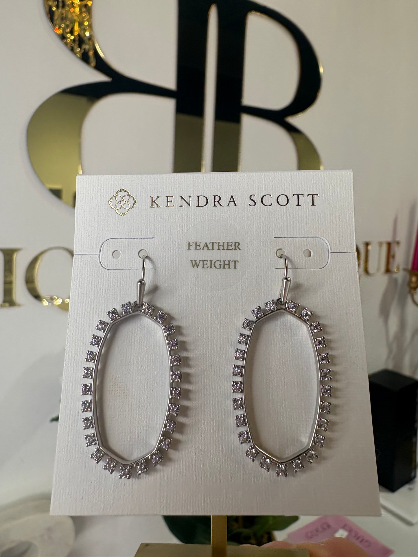 Kendra Scott feather weight earrings on a display card with a blurred background.