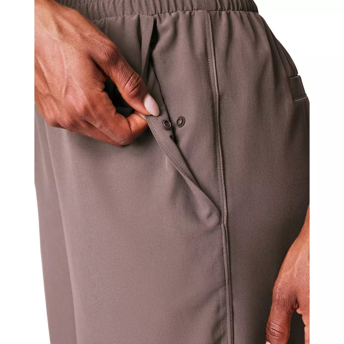 Close-up of a person wearing gray pants with a button detail on a white background