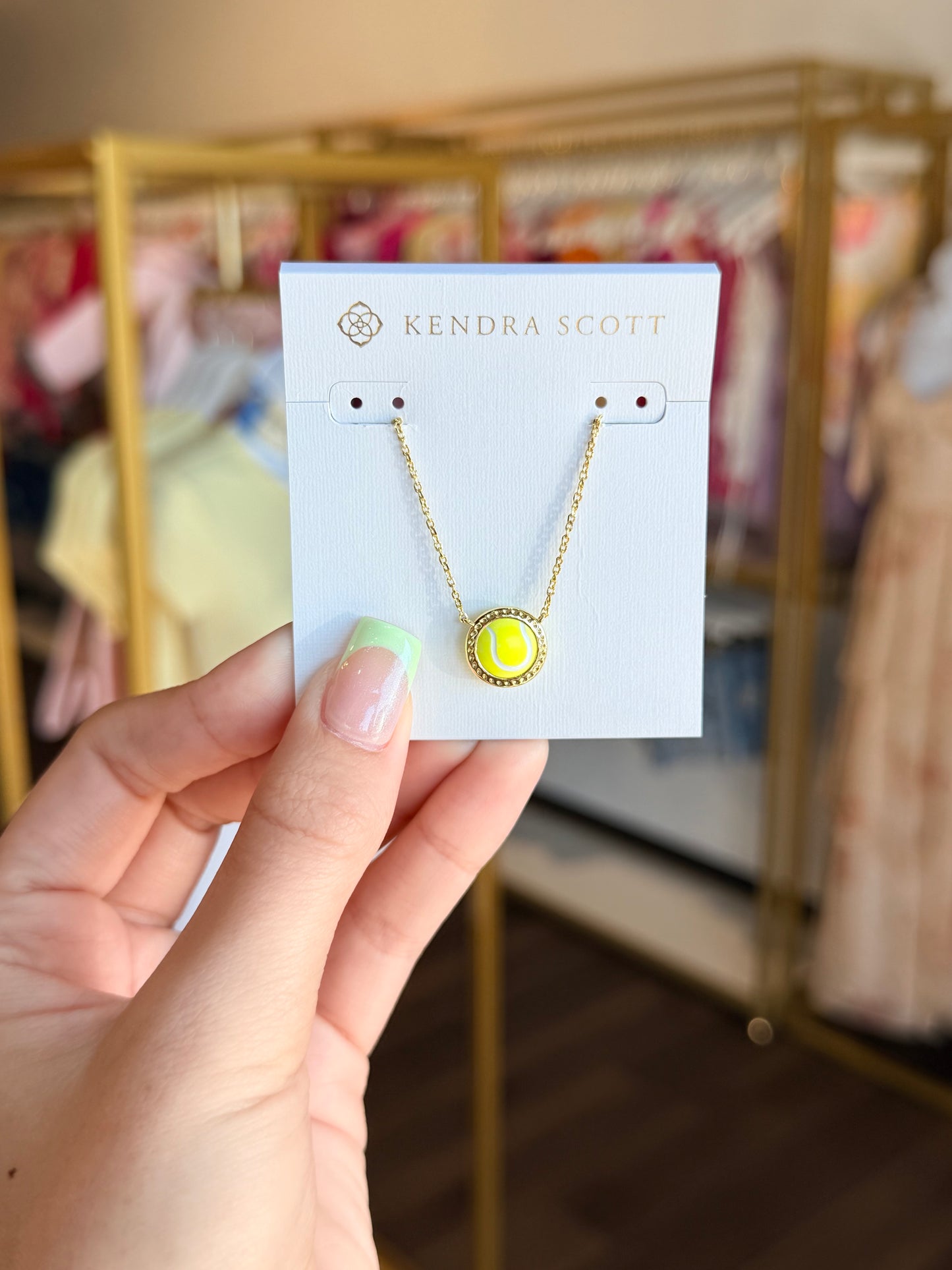 Kendra Scott necklace on a card held by a hand with a blurred store background