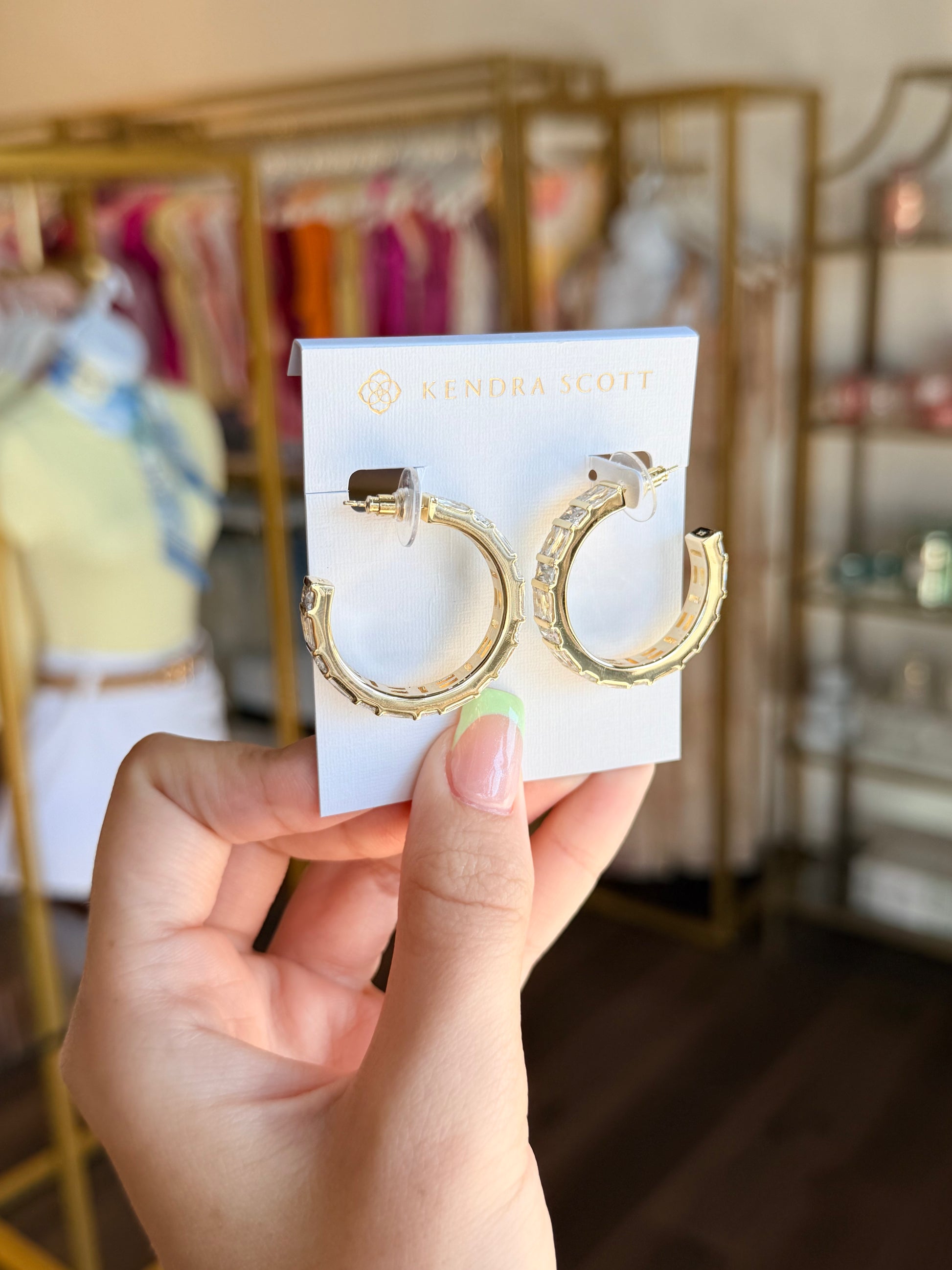 Gold hoop earrings on a Kendra Scott card held by a hand in a store setting.