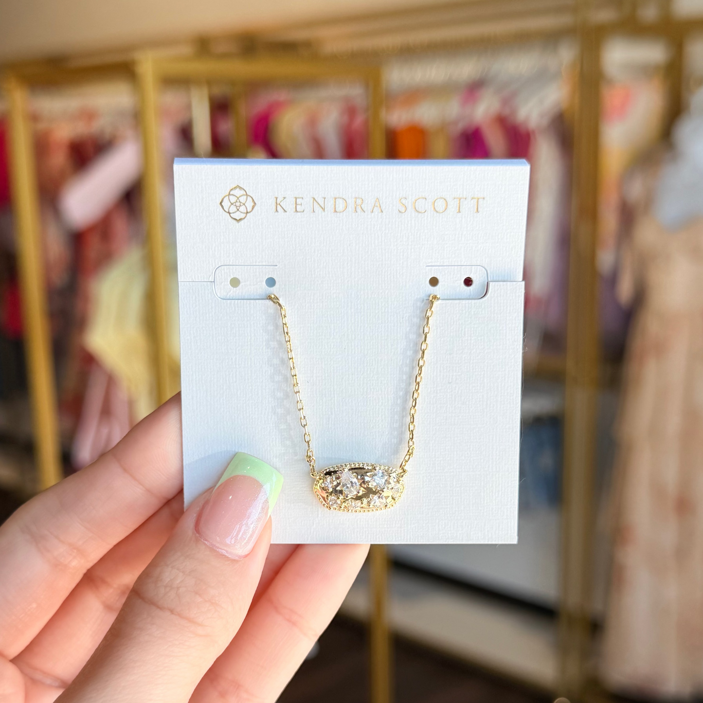 Hand holding a Kendra Scott necklace card with a blurred store background