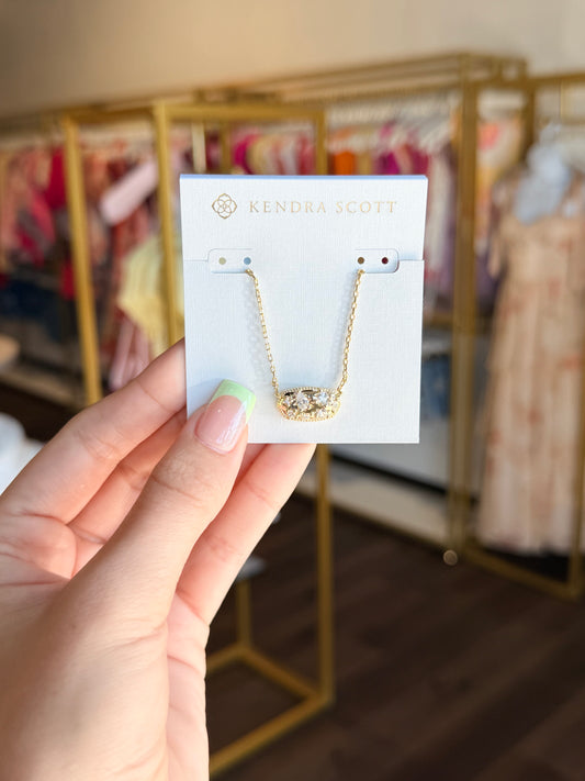 Hand holding a Kendra Scott necklace card with a blurred store background