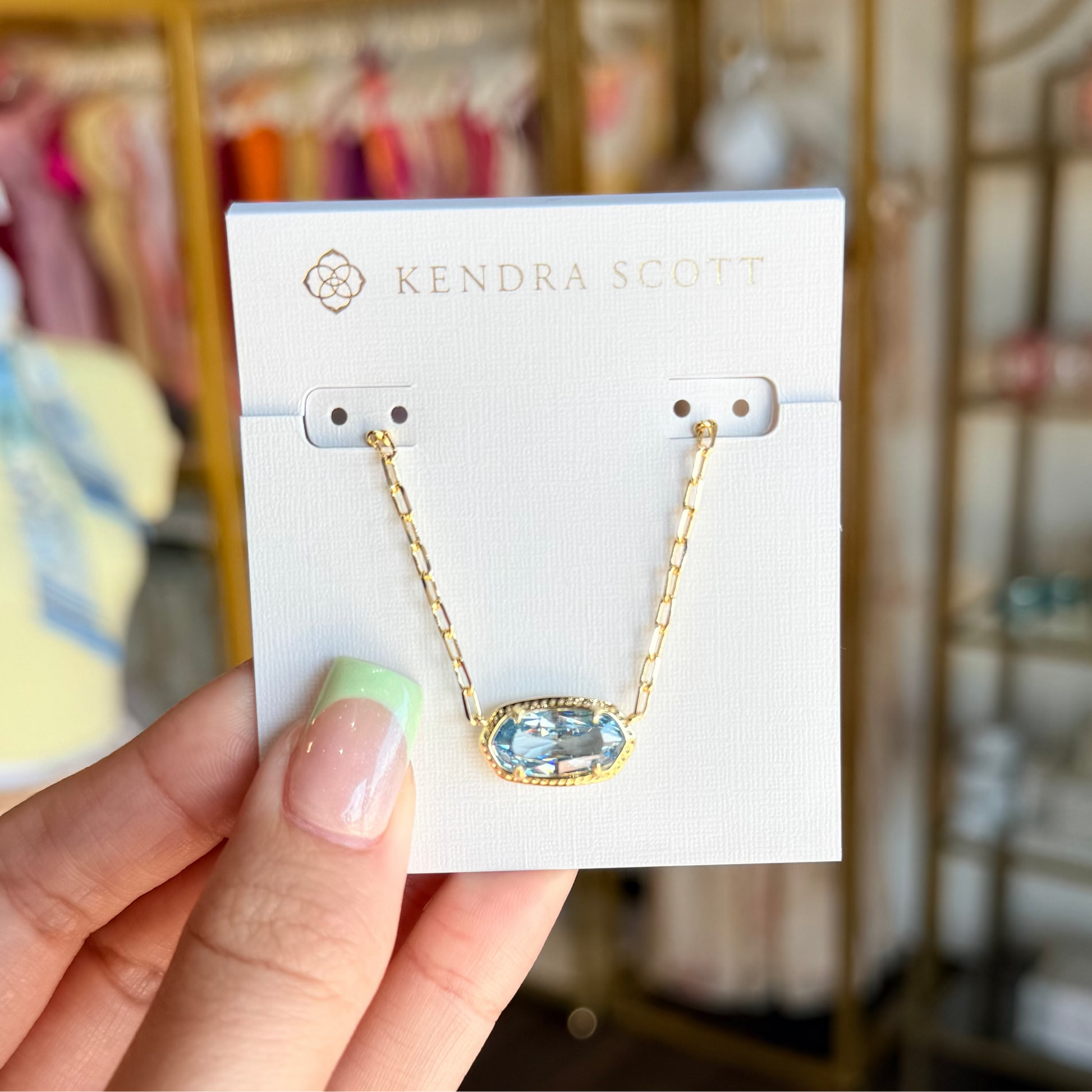 Hand holding a pair of earrings on a Kendra Scott card with a blurred store background
