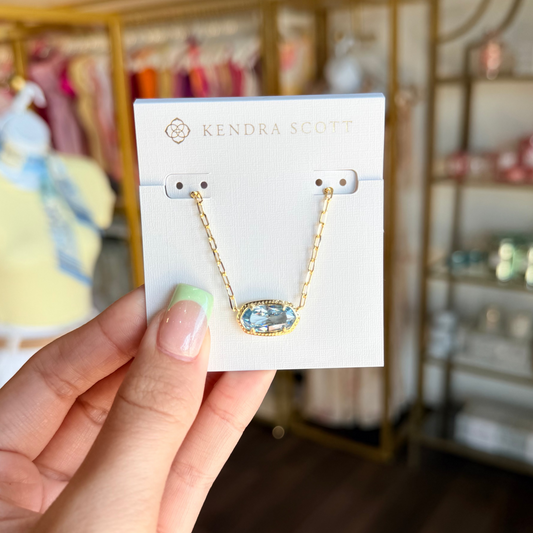 Hand holding a pair of earrings on a Kendra Scott card with a blurred store background