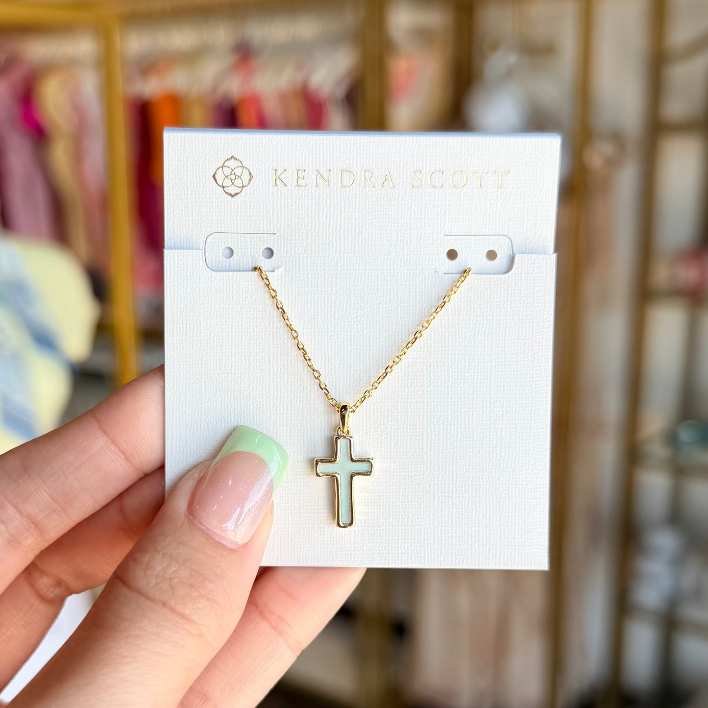 Gold cross necklace on a display card held by a hand with a blurred store background