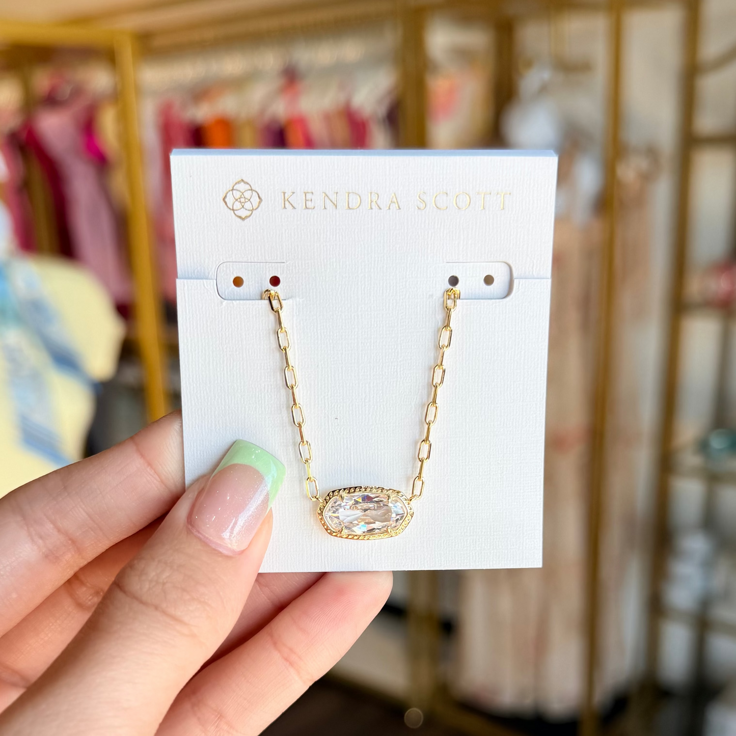 Hand holding a card with a gold necklace and earrings on a blurred store background