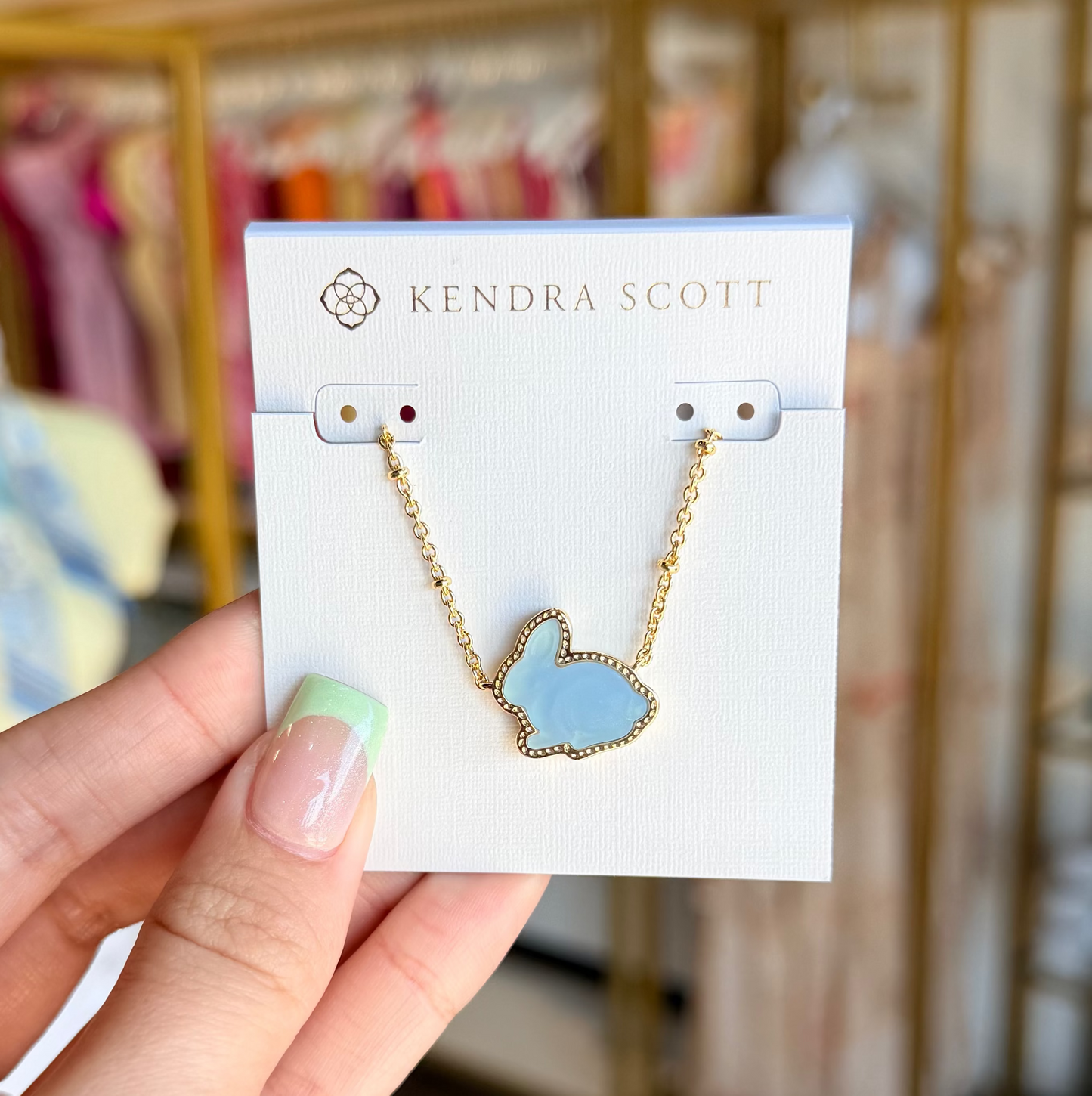 Hand holding a Kendra Scott necklace card with a blurred store background