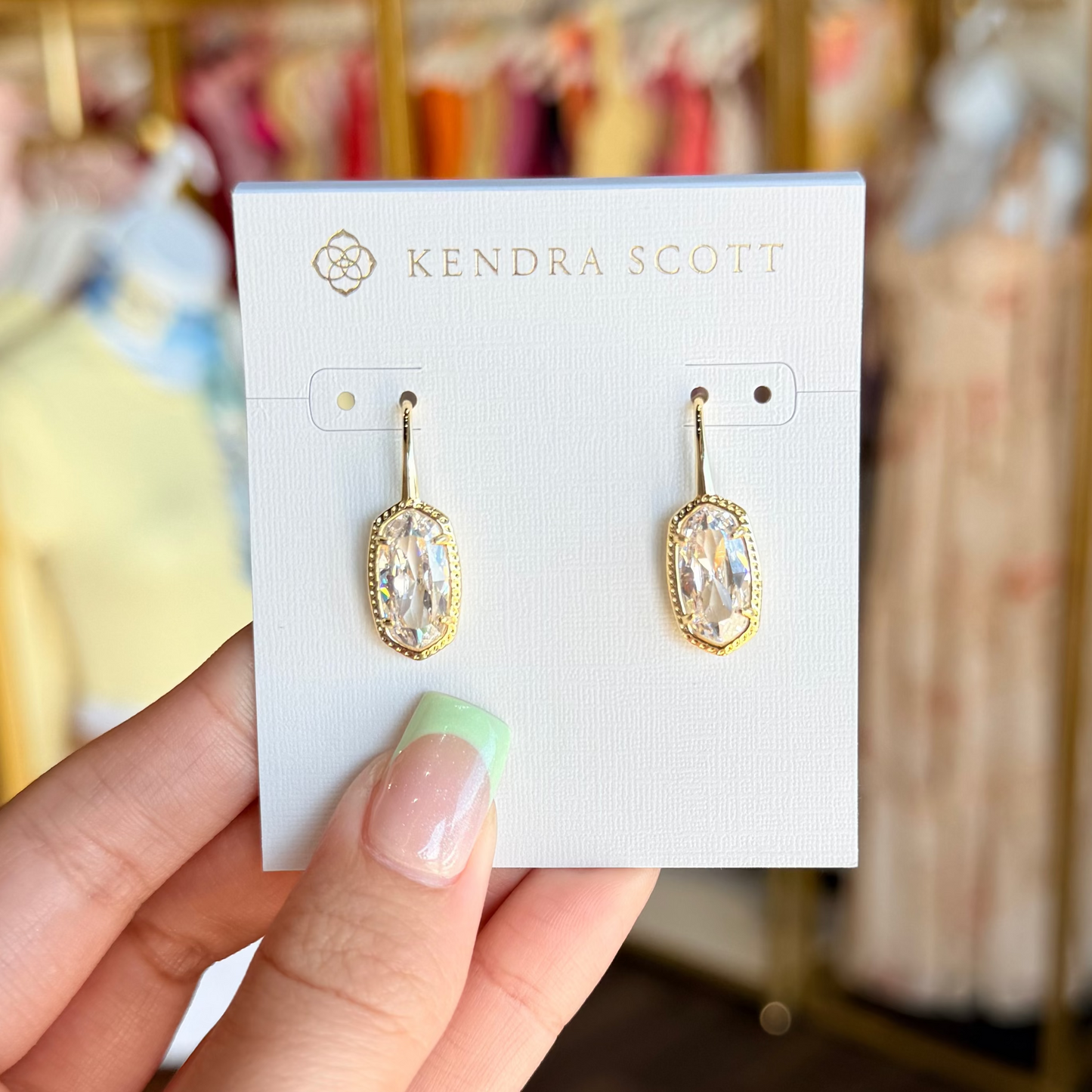 Gold earrings on a Kendra Scott card held by a hand with a blurred store background