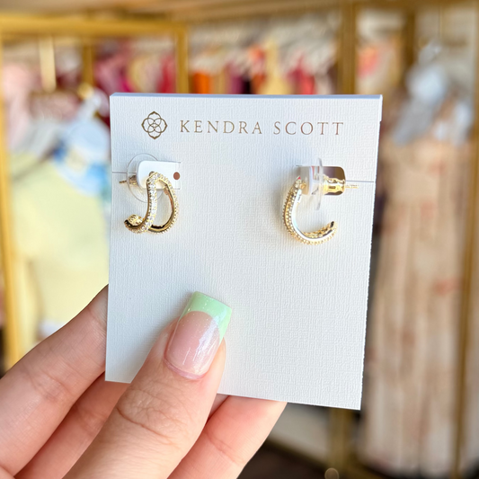 Gold hoop earrings on a Kendra Scott card held by a hand with a blurred store background.