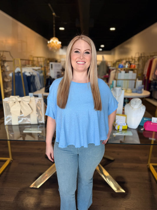 Woman in a blue top and jeans standing in a store with clothing racks and displays.