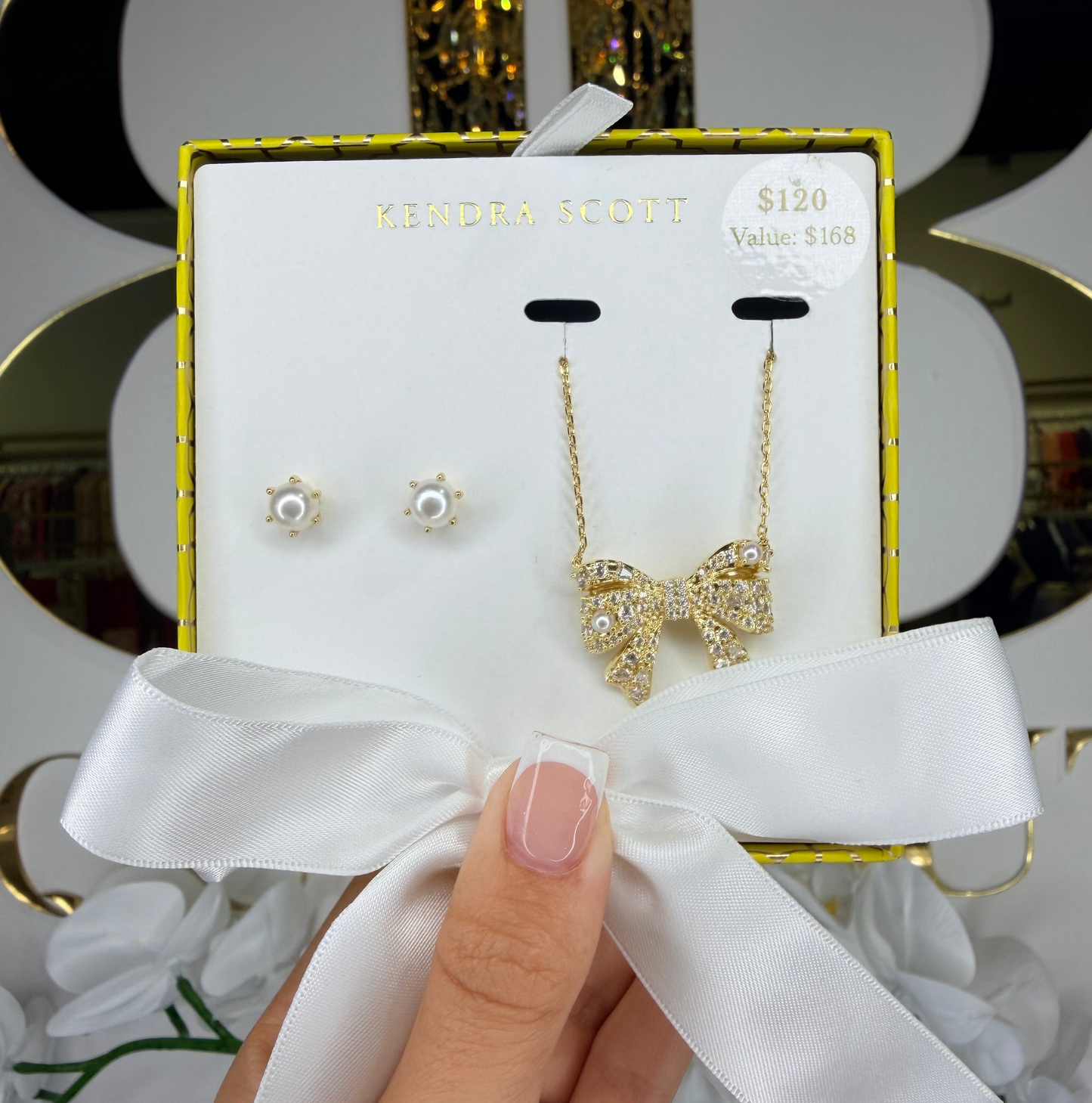 Gold bow-shaped earrings on a card with a white ribbon held by a hand.