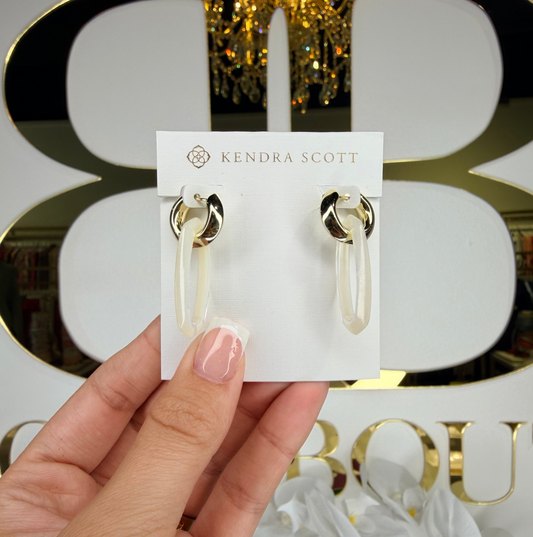 Kendra Scott earrings held in front of a decorative background