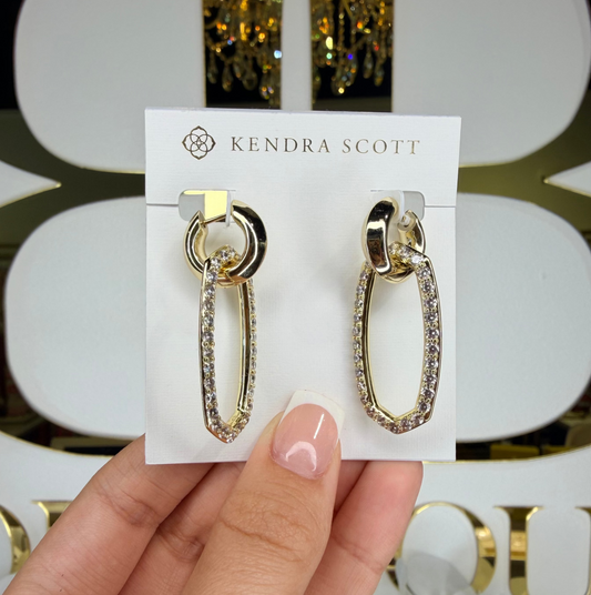 Gold hoop earrings on a Kendra Scott card held by a hand against a decorative background.