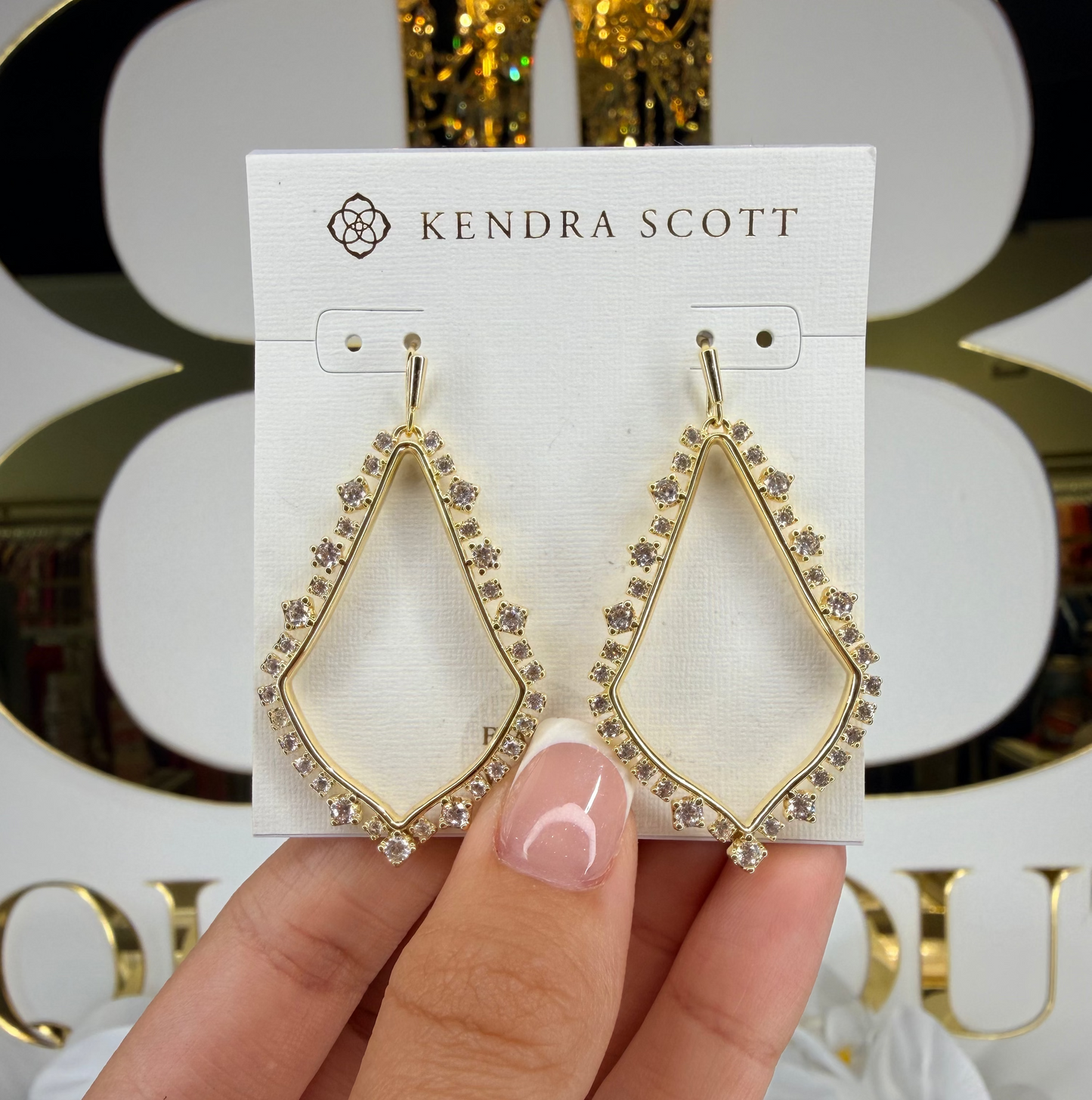 Hand holding Kendra Scott gold dangling earrings 
