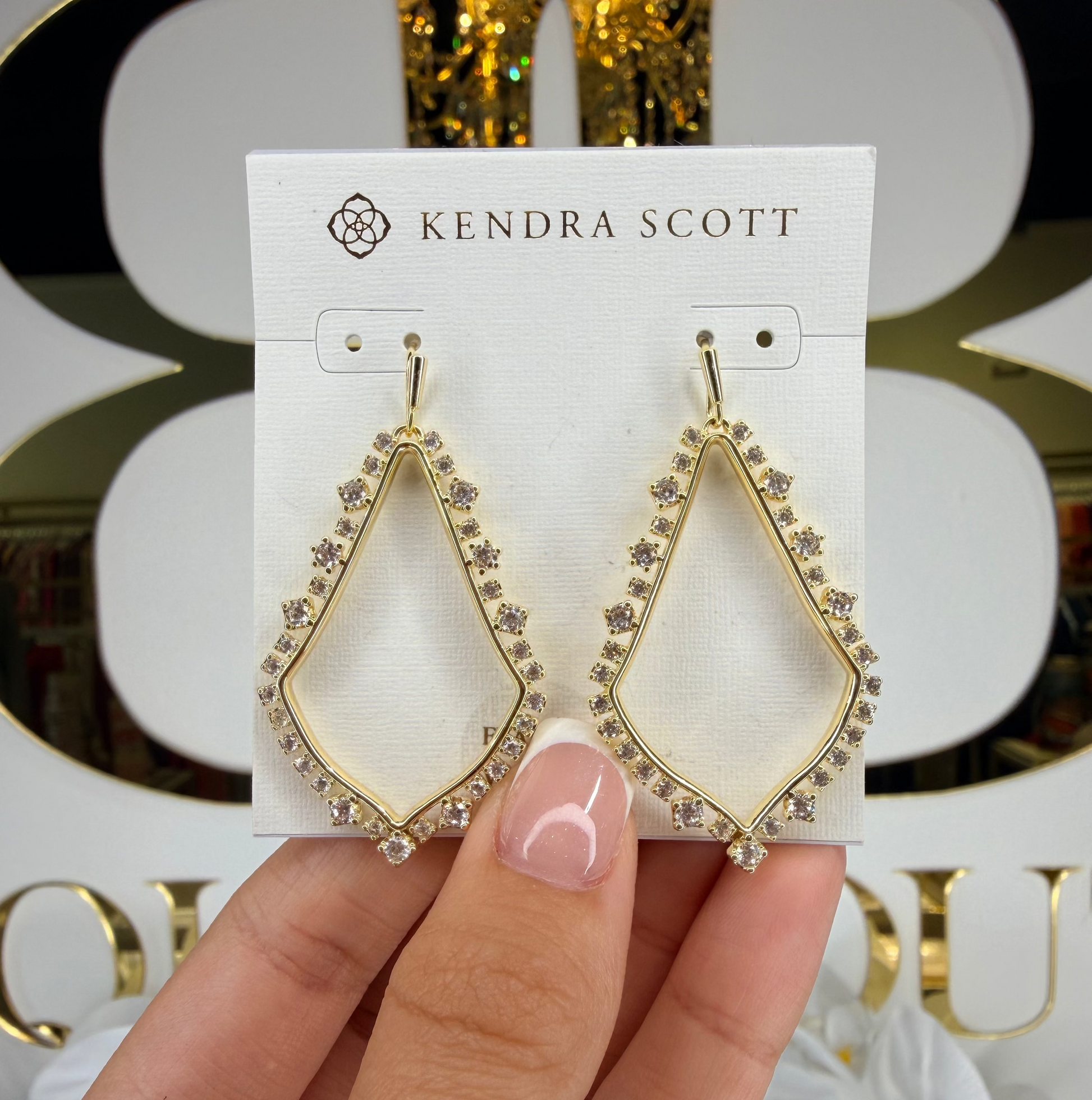 Hand holding Kendra Scott gold dangling earrings 
